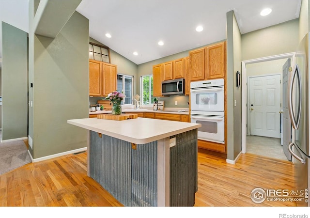 kitchen with appliances with stainless steel finishes, baseboards, light countertops, light wood-type flooring, and a center island
