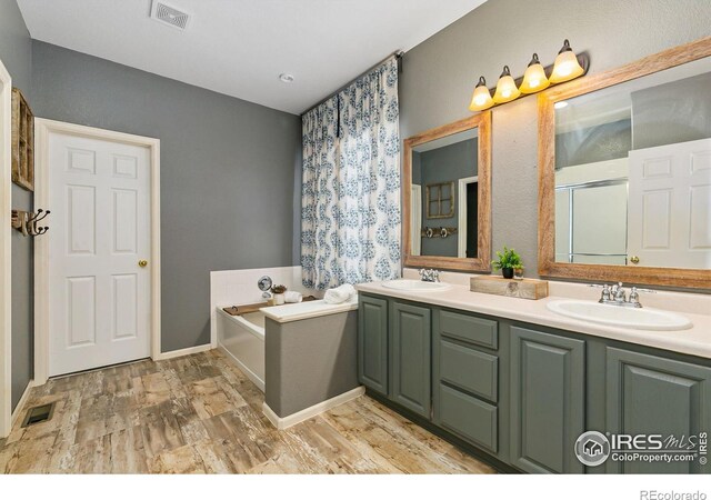 full bathroom with a garden tub, wood finished floors, double vanity, and a shower with shower door