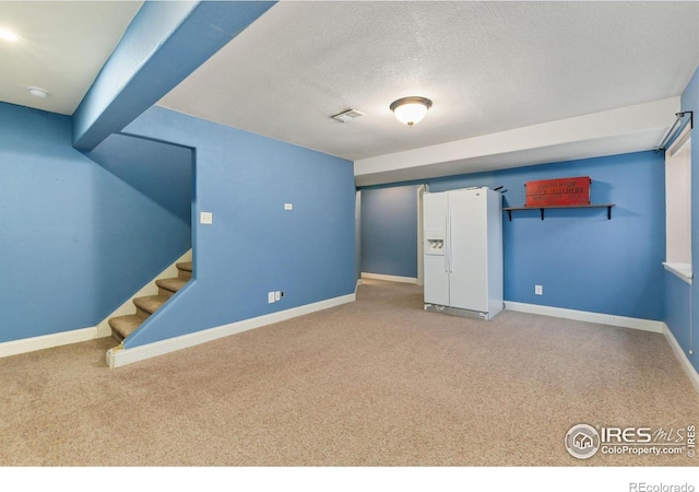 finished below grade area with white fridge with ice dispenser, carpet flooring, baseboards, stairway, and a textured ceiling