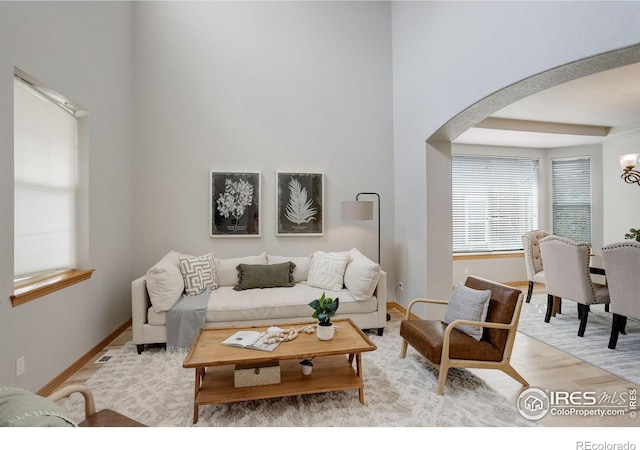 living area featuring arched walkways, wood finished floors, baseboards, and a chandelier