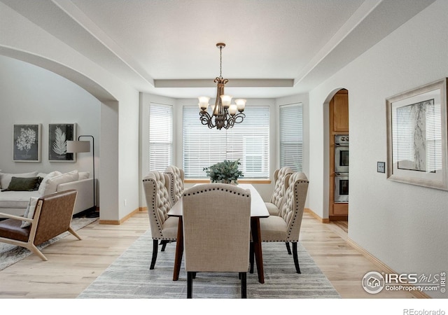 dining space with arched walkways, a chandelier, a tray ceiling, light wood-style floors, and baseboards