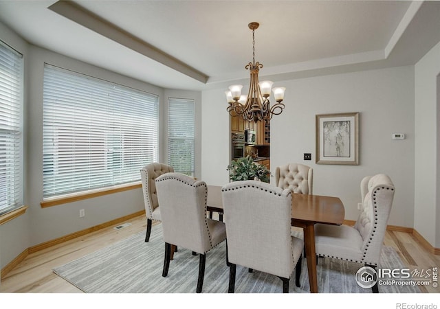 dining room featuring a tray ceiling, light wood-style floors, a chandelier, and baseboards