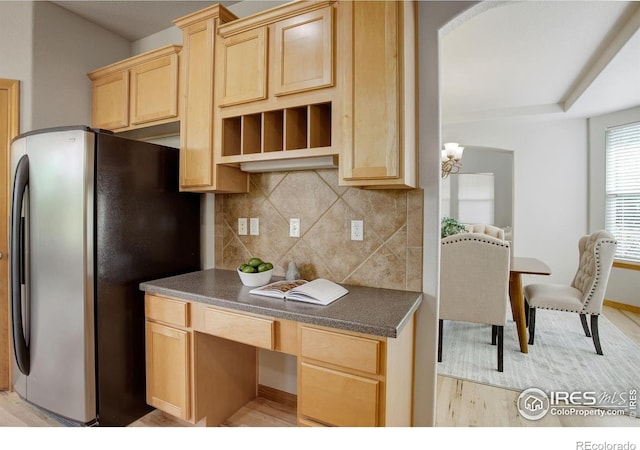 kitchen featuring freestanding refrigerator, light brown cabinetry, dark countertops, and backsplash