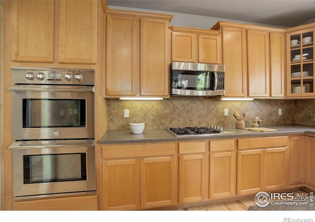 kitchen featuring stainless steel appliances, glass insert cabinets, backsplash, and light brown cabinets