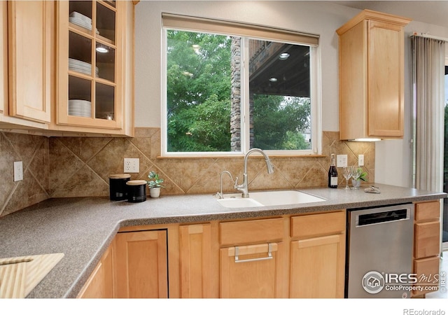 kitchen featuring light brown cabinetry, a sink, stainless steel dishwasher, glass insert cabinets, and tasteful backsplash