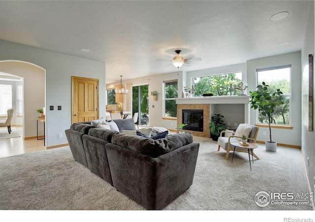 carpeted living area featuring arched walkways, a tiled fireplace, baseboards, and ceiling fan