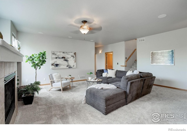 carpeted living room with stairway, a tiled fireplace, ceiling fan, and baseboards