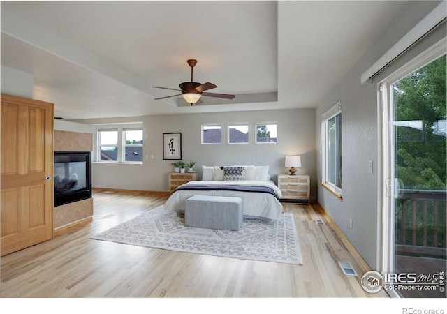 bedroom with light wood-style floors, a multi sided fireplace, and a ceiling fan