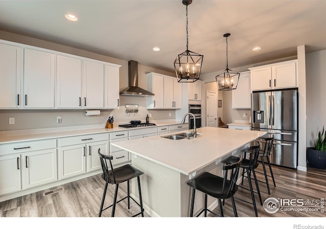 kitchen with stainless steel appliances, a sink, wall chimney range hood, wood finished floors, and a kitchen bar