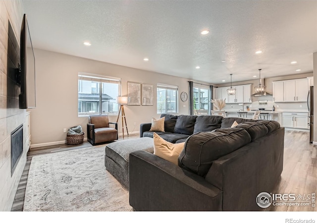 living area with recessed lighting, light wood-type flooring, a fireplace, a textured ceiling, and baseboards