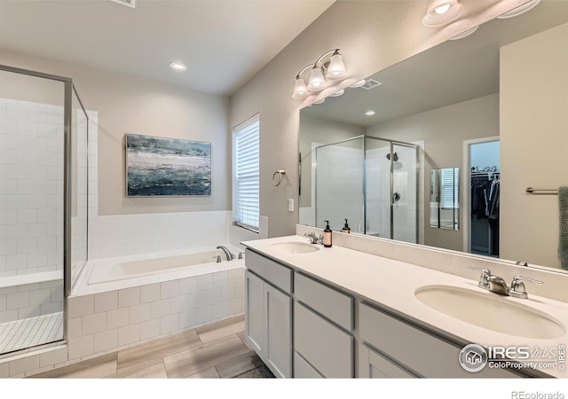 bathroom with a stall shower, a bath, a spacious closet, double vanity, and recessed lighting