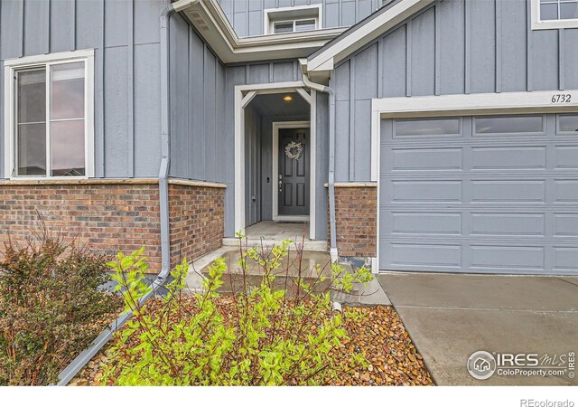 view of exterior entry with board and batten siding, brick siding, and an attached garage