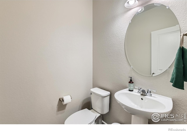 bathroom with a sink, toilet, and a textured wall