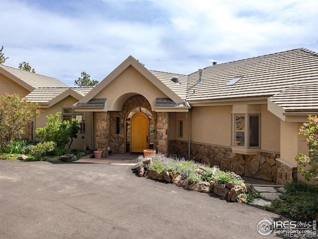 view of front of property with stone siding, stucco siding, and a tile roof