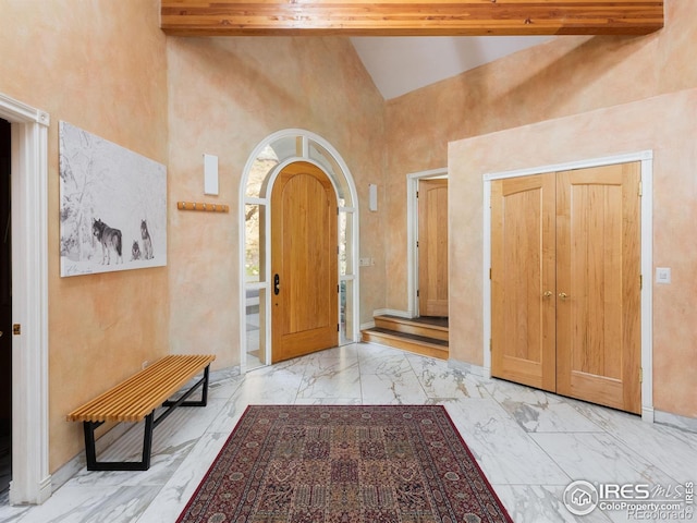 foyer featuring marble finish flooring, high vaulted ceiling, and baseboards