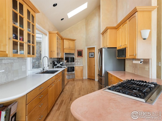 kitchen with a sink, appliances with stainless steel finishes, a skylight, light wood-style floors, and high vaulted ceiling