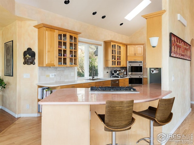kitchen with a sink, appliances with stainless steel finishes, vaulted ceiling, backsplash, and light wood finished floors