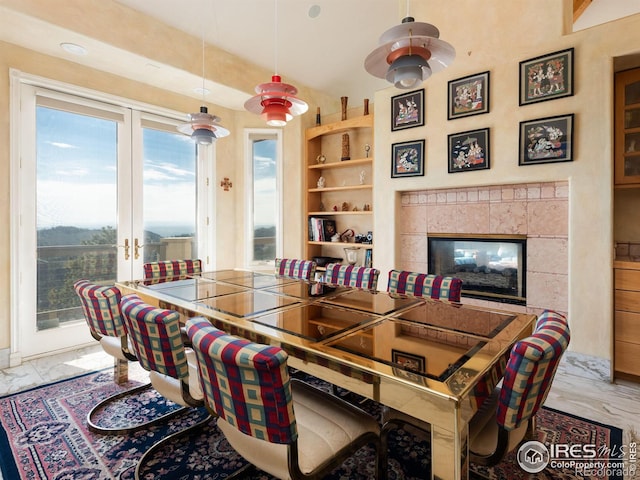 dining space with light marble finish floors, a tile fireplace, plenty of natural light, and french doors