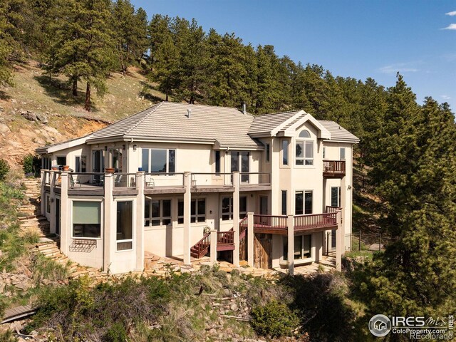 rear view of property with a balcony, a tile roof, stairs, and stucco siding
