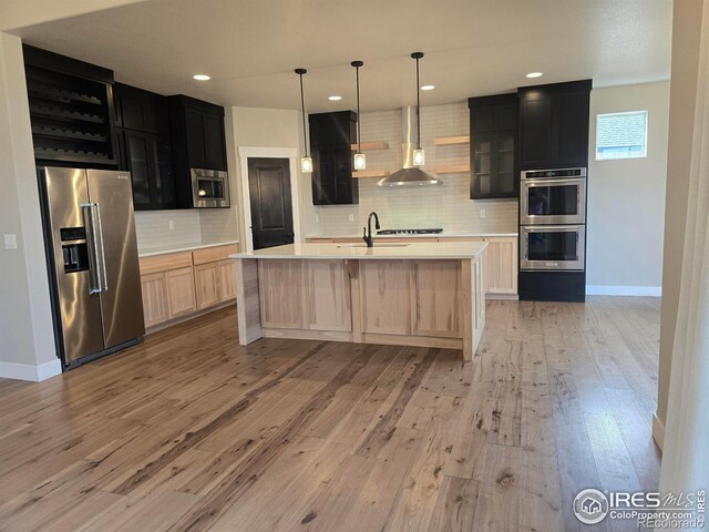 kitchen featuring appliances with stainless steel finishes, wall chimney exhaust hood, dark cabinets, light countertops, and decorative backsplash