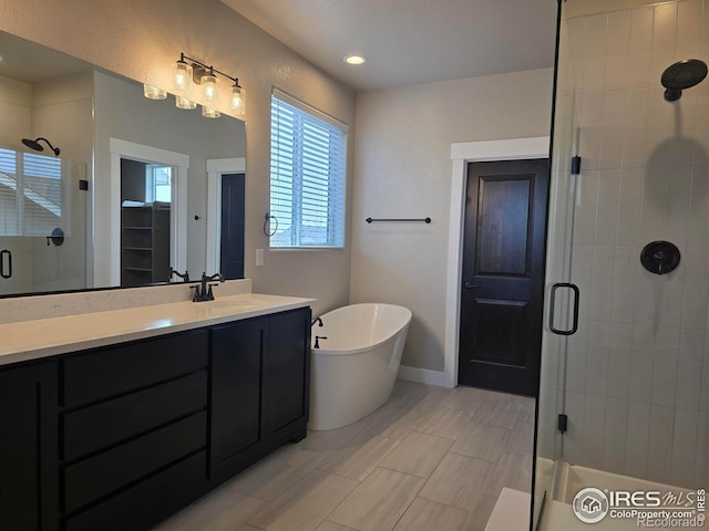 bathroom featuring a shower stall, a freestanding bath, vanity, baseboards, and a spacious closet