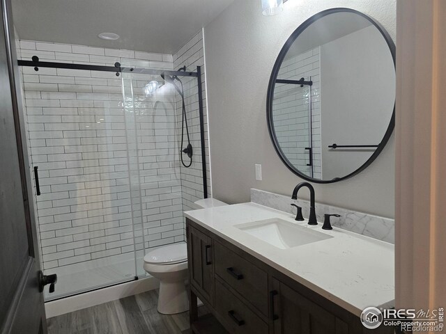 bathroom featuring a stall shower, wood finished floors, toilet, and vanity