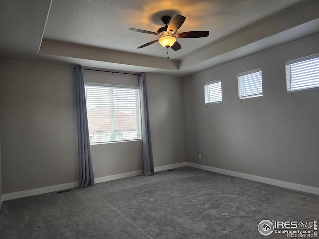 spare room with a tray ceiling, carpet floors, ceiling fan, and baseboards