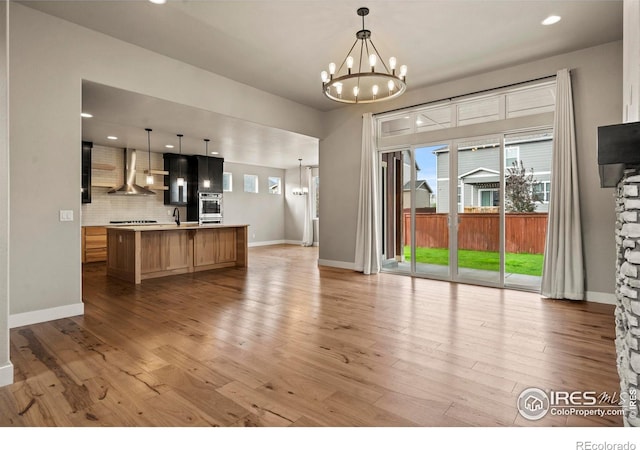 1940 Rolling Wind Dr, Windsor, CO 80550 - kitchen featuring wall chimney range hood, stainless steel oven, a chandelier, open floor plan, and light countertops