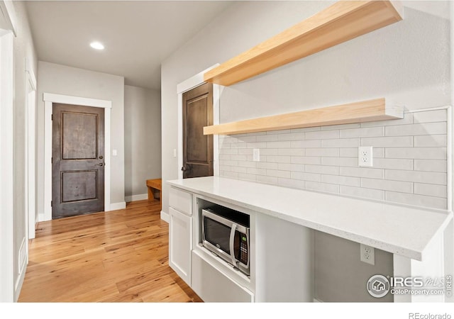 1940 Rolling Wind Dr, Windsor, CO 80550 - kitchen featuring stainless steel microwave, open shelves, light wood finished floors, white cabinets, and decorative backsplash