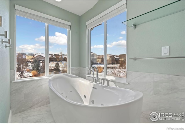 full bath with marble look tiles, tile walls, a freestanding bath, and healthy amount of natural light