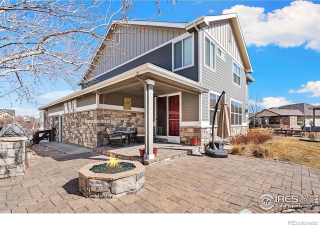back of property featuring board and batten siding, stone siding, an outdoor fire pit, and a patio area