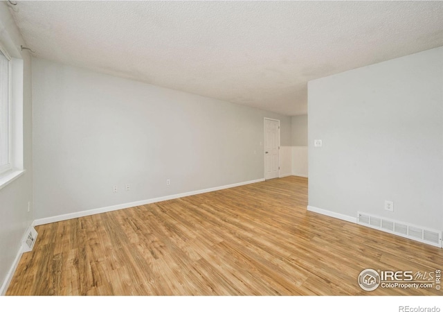 empty room with light wood finished floors, a textured ceiling, and baseboards