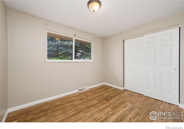 unfurnished bedroom with wood finished floors, baseboards, a closet, and a textured ceiling