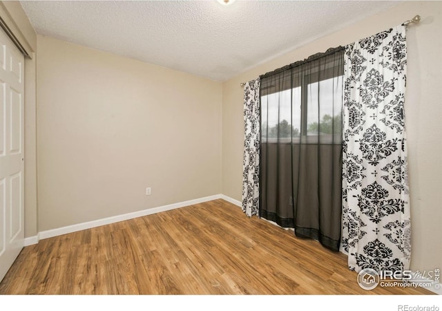 spare room featuring light wood-type flooring, baseboards, and a textured ceiling