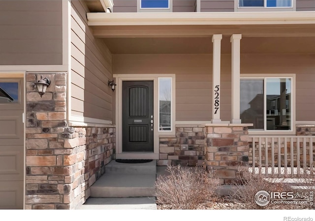 view of exterior entry with stone siding and covered porch