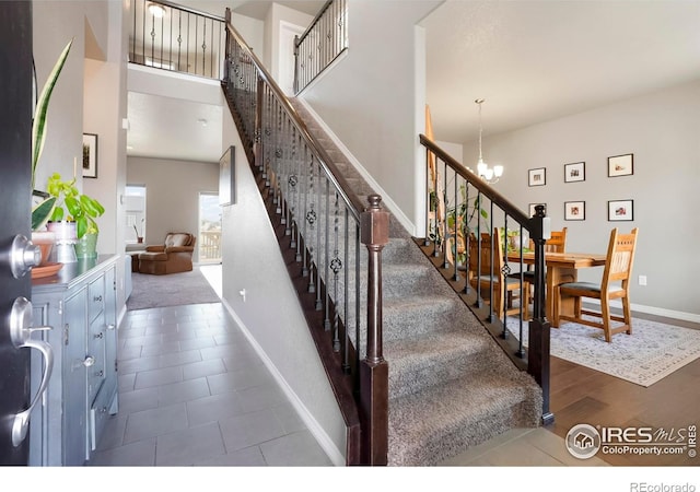 staircase with a chandelier, baseboards, a high ceiling, and tile patterned floors