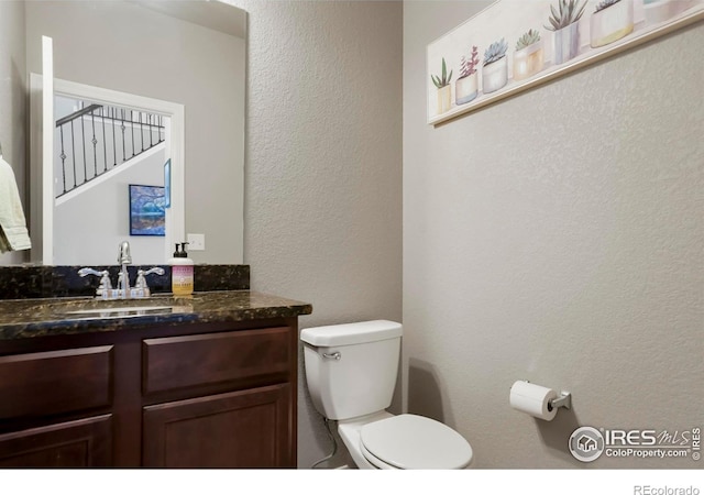 bathroom featuring a textured wall, vanity, and toilet