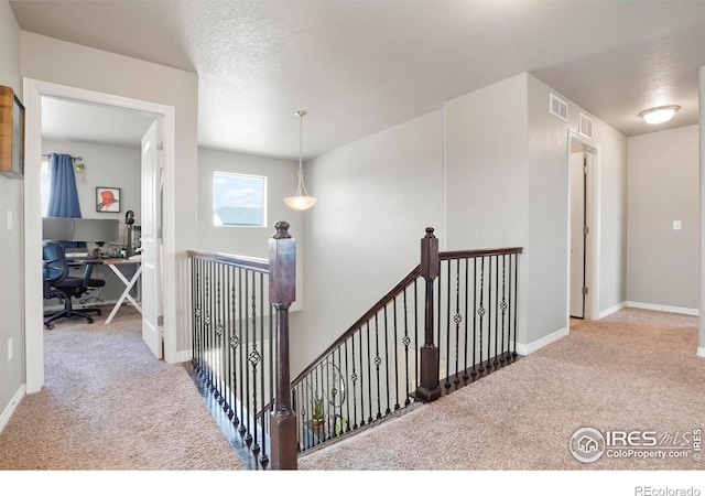 hall featuring carpet, an upstairs landing, a desk, and baseboards