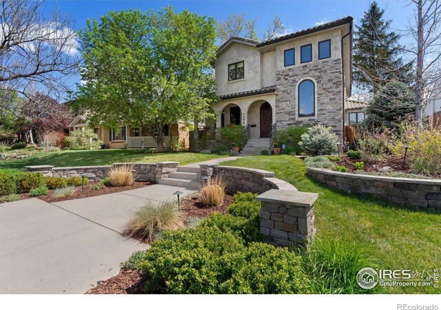 mediterranean / spanish-style home featuring stone siding, stucco siding, a front yard, and a tiled roof