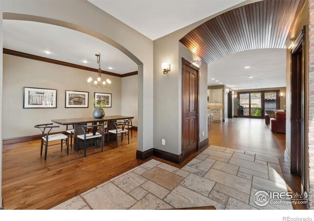 hallway with arched walkways, baseboards, recessed lighting, stone tile floors, and a chandelier