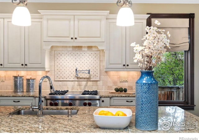 kitchen with a sink, light stone countertops, tasteful backsplash, and hanging light fixtures