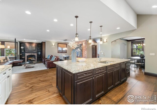 kitchen with a lit fireplace, a sink, arched walkways, light wood-type flooring, and dark brown cabinets