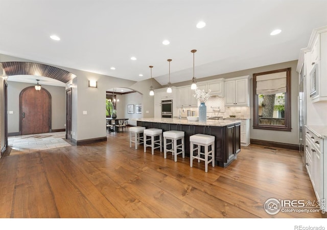 kitchen with arched walkways, wood finished floors, a large island with sink, a kitchen breakfast bar, and white cabinetry