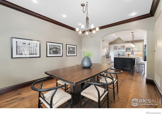 dining space featuring arched walkways, dark wood-style flooring, ornamental molding, a chandelier, and recessed lighting