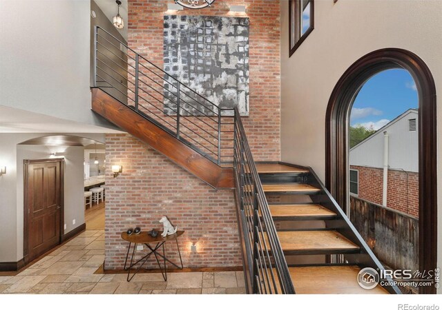 stairway with a towering ceiling, plenty of natural light, stone tile flooring, baseboards, and arched walkways