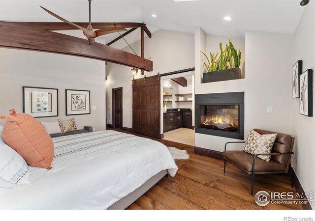 bedroom with wood finished floors, high vaulted ceiling, a glass covered fireplace, a barn door, and baseboards