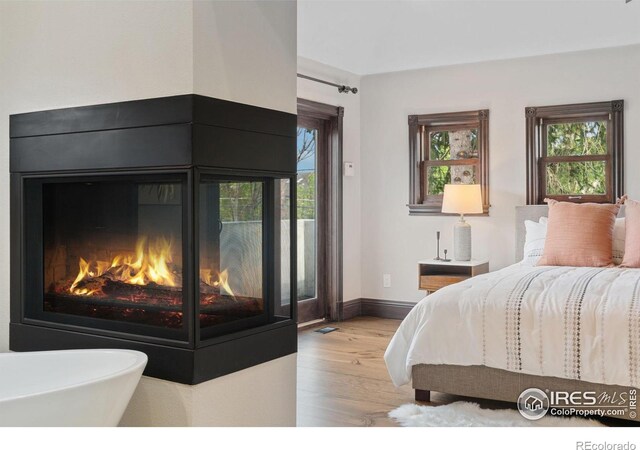 bedroom with a multi sided fireplace, light wood-style floors, access to outside, and baseboards