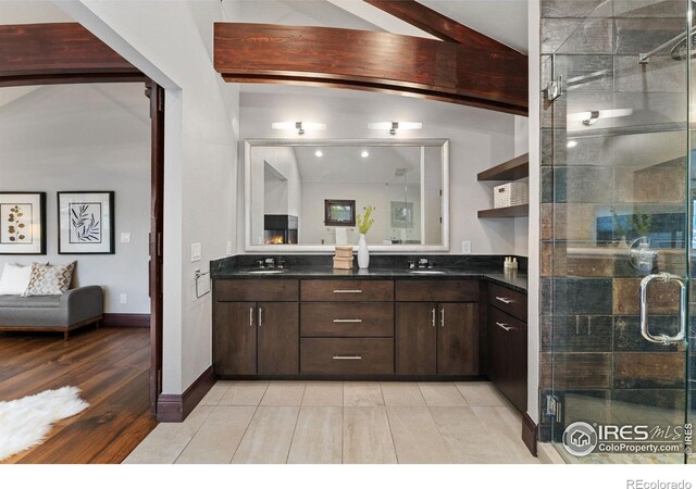 bathroom with a stall shower, double vanity, beam ceiling, and baseboards