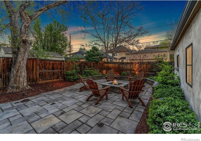 patio terrace at dusk featuring a fire pit and a fenced backyard