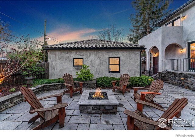 patio terrace at dusk featuring an outdoor fire pit and fence